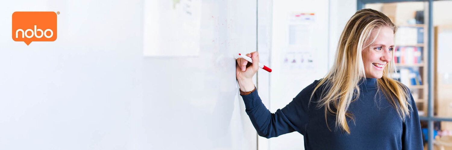 Nainen kirjoittaa valkotaululle ja hymyilee.