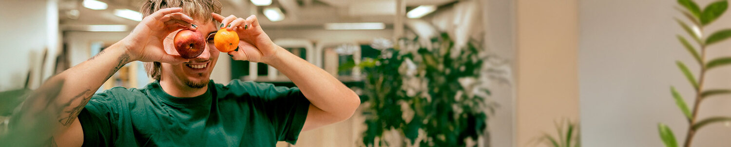 Kaksi nuorta toimistolla, toisella omena ja appelsiini silmien edessä