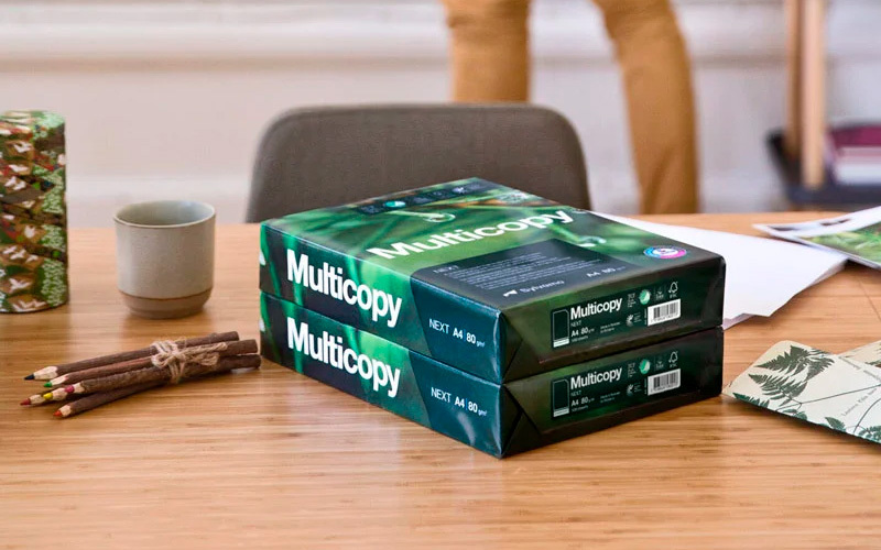 Työpöydällä Multicopy kopiopapeririisi, kahvikuppi, kynä ja muita toimistotarvikkeita.