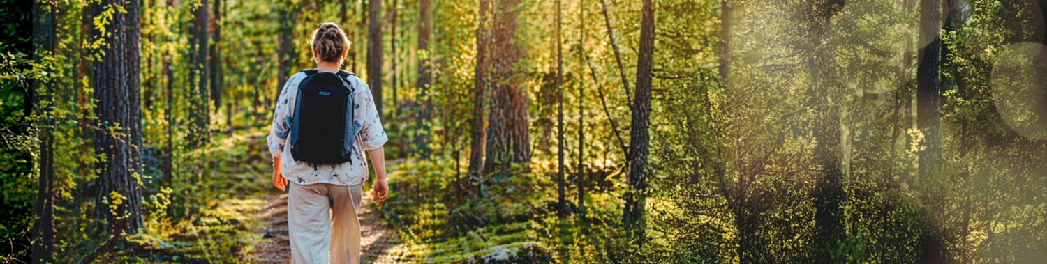 Nuori ihminen kävelee metsäpolulla reppu selässään.